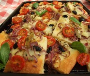 Gluten free pizza with tomatoes, olives, artichokes, onion, and mozzarella